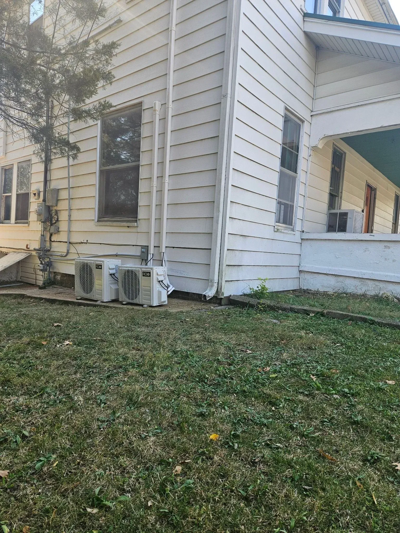 Side of a white house with air conditioning unit on the ground, window, and porch.