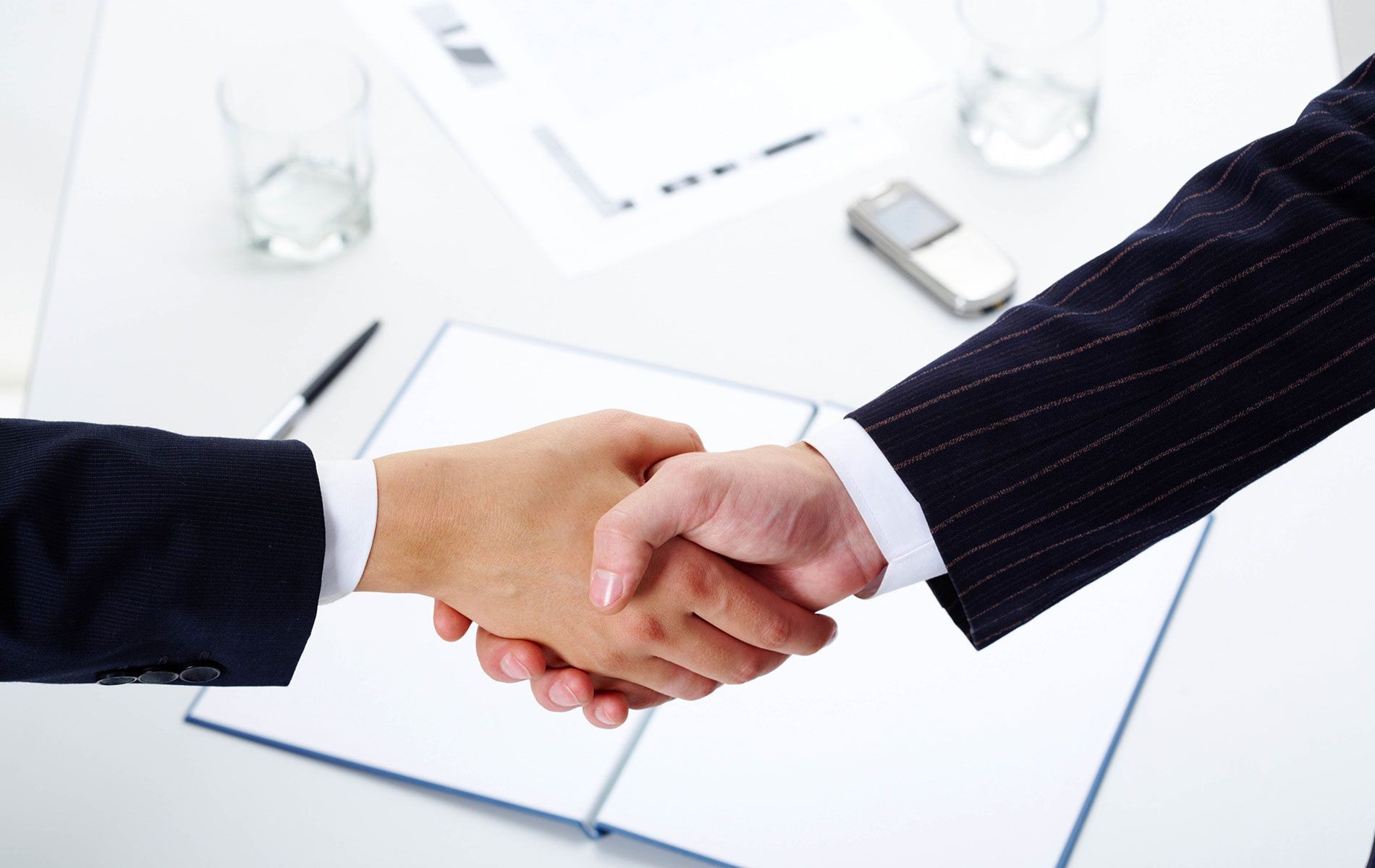 Two people shaking hands over an open notebook on a white table.