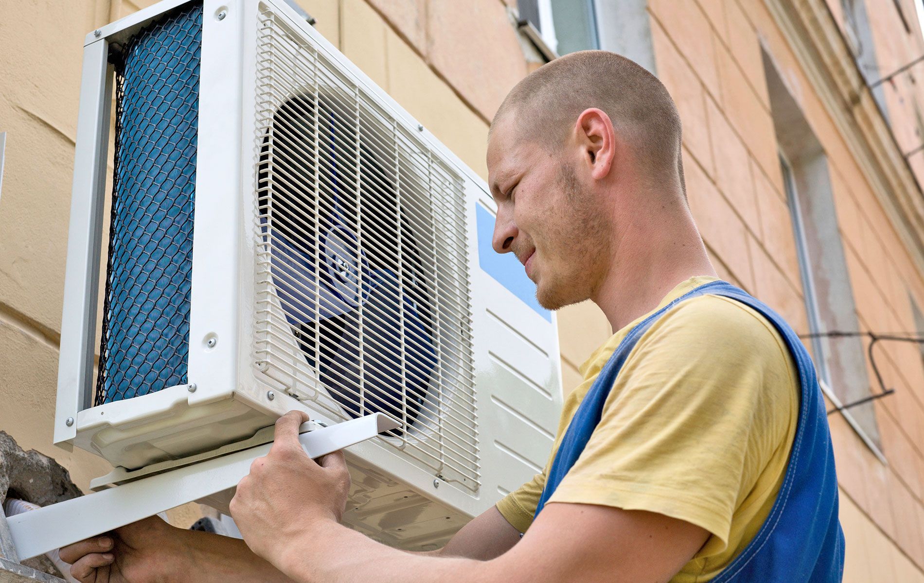 Man installing an air conditioning unit on an exterior wall.
