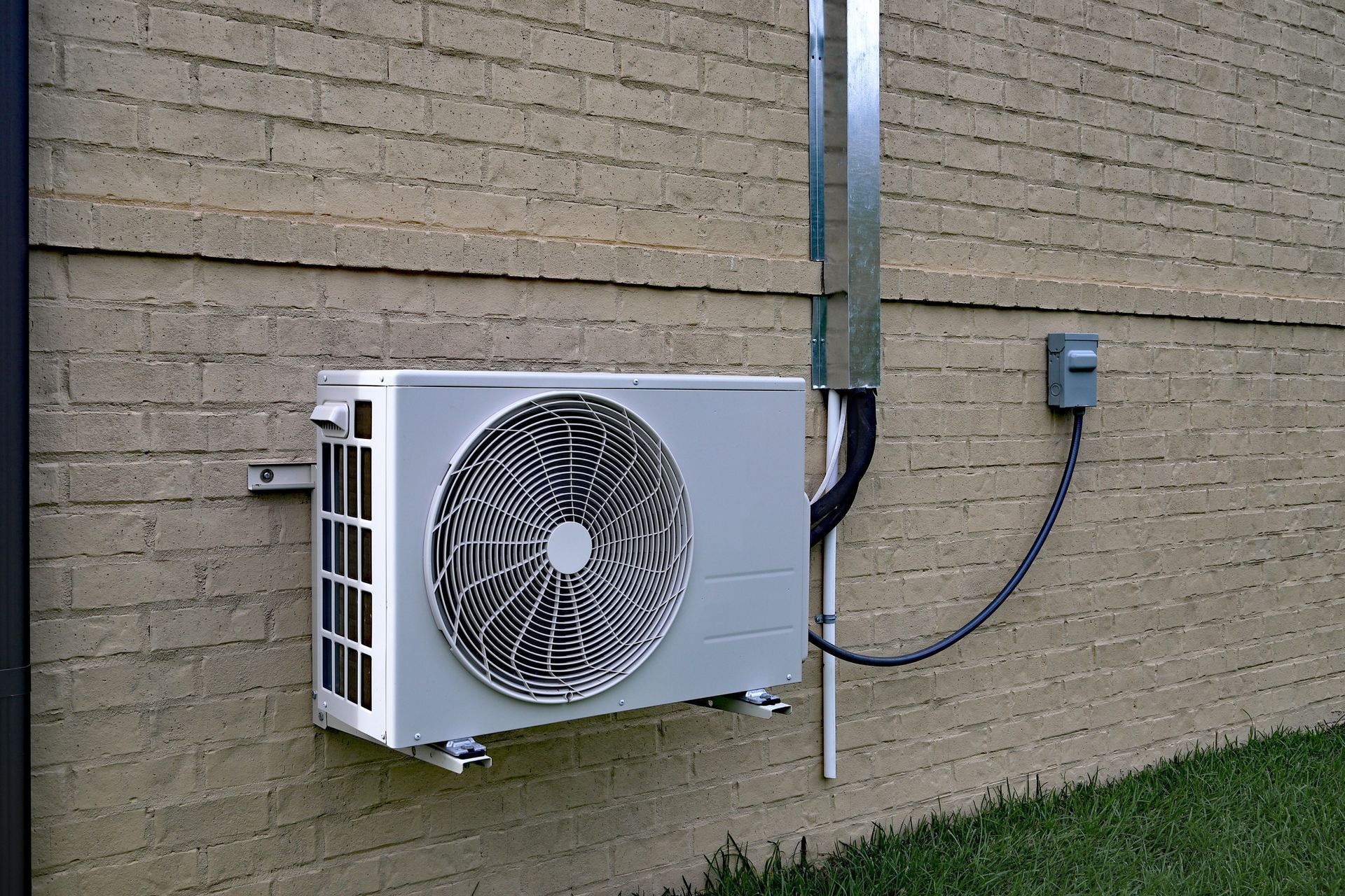 Air conditioning unit mounted on a brick wall with electrical conduit and outlet.