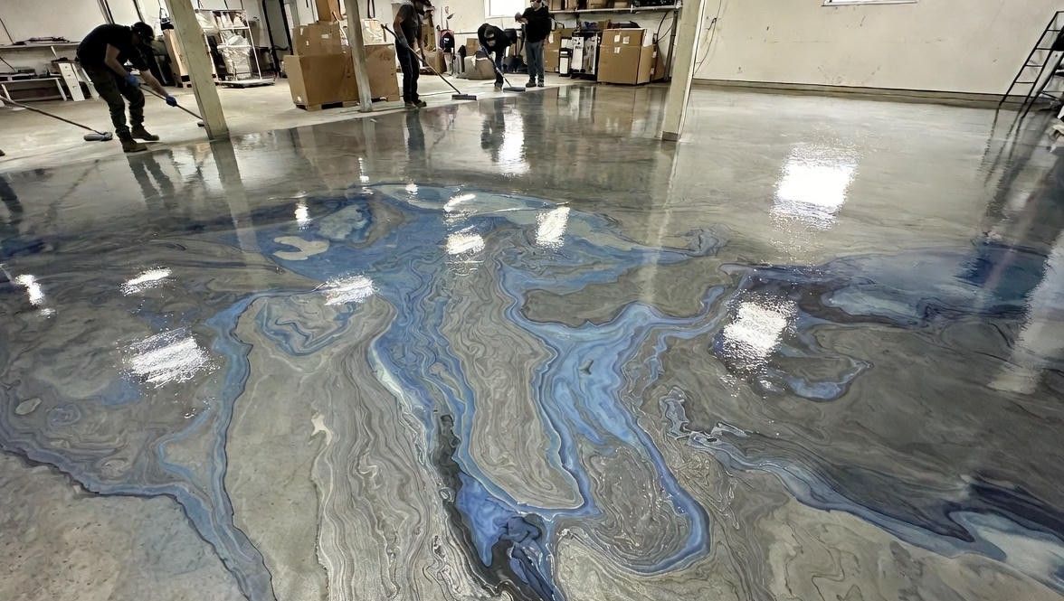 Workers applying epoxy floor coating in a large room; swirling silver and blue pattern.