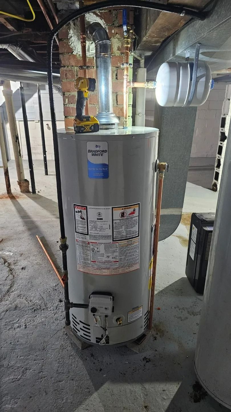 A vertical, gray water heater in a basement setting, with copper pipes and a vent.