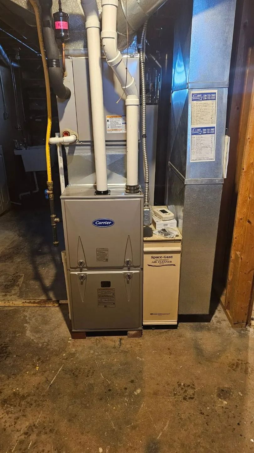 Furnace unit with ductwork in a basement setting. The furnace is light gray with white pipes.