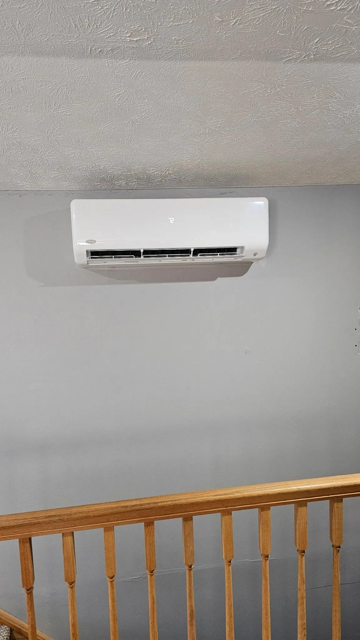 White air conditioning unit mounted on a gray wall above wooden stairs.