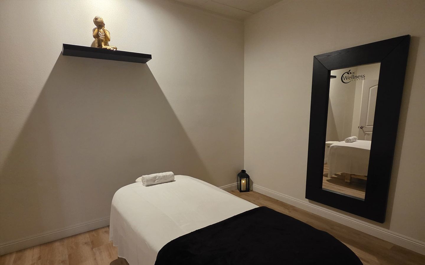 Massage room with massage table, mirror, shelf with buddha, and a candle.