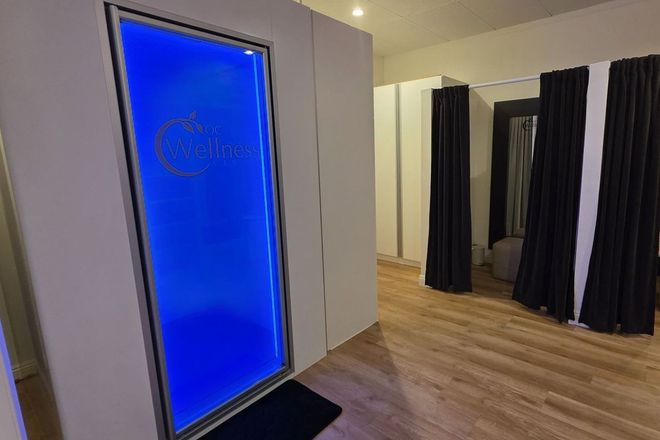 A white-walled room with a blue-lit, framed sign. Dark curtains hang in the background with wooden floors.