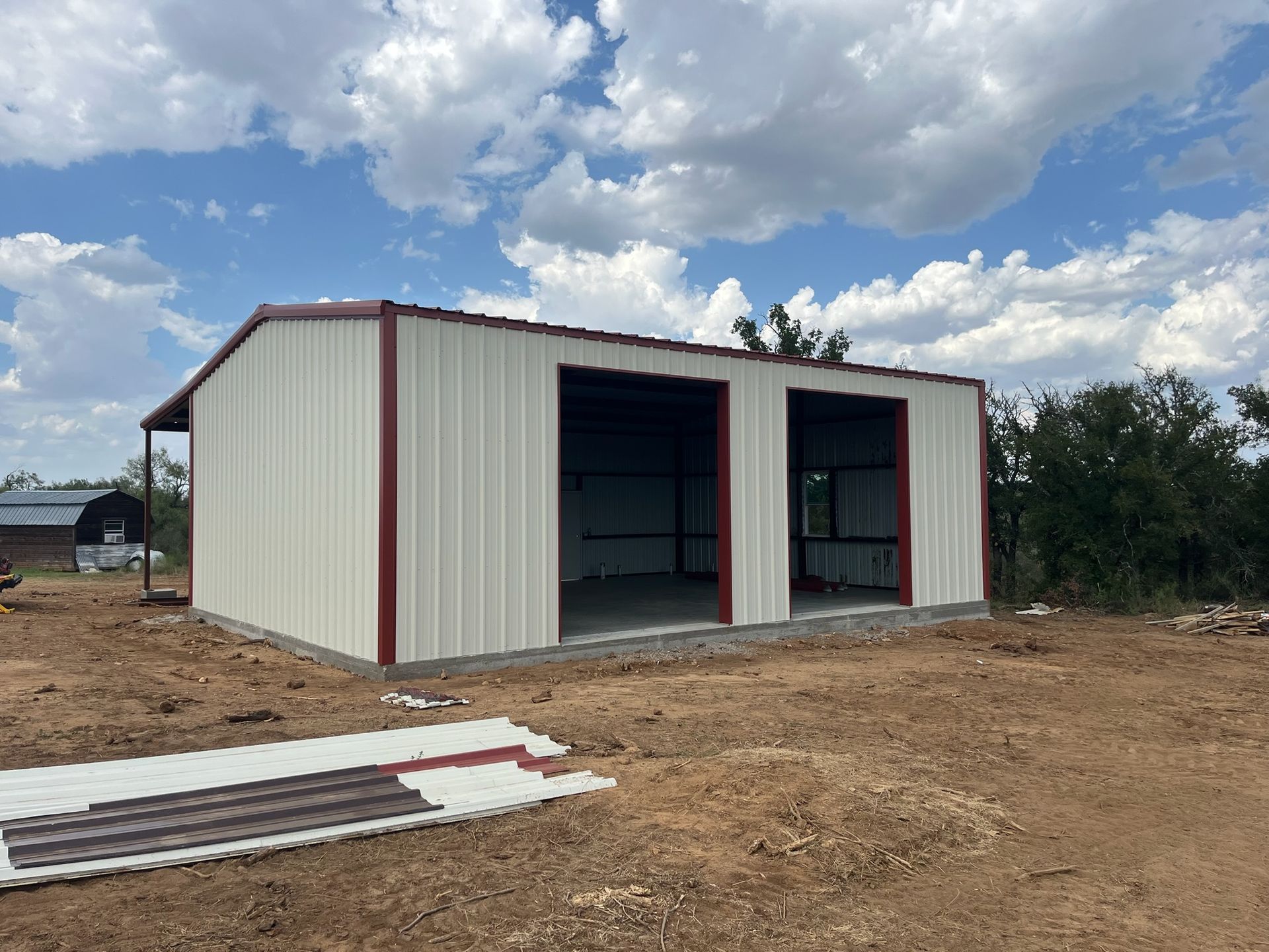 Small white metal storage building with red trim on a dirt lot under a cloudy sky