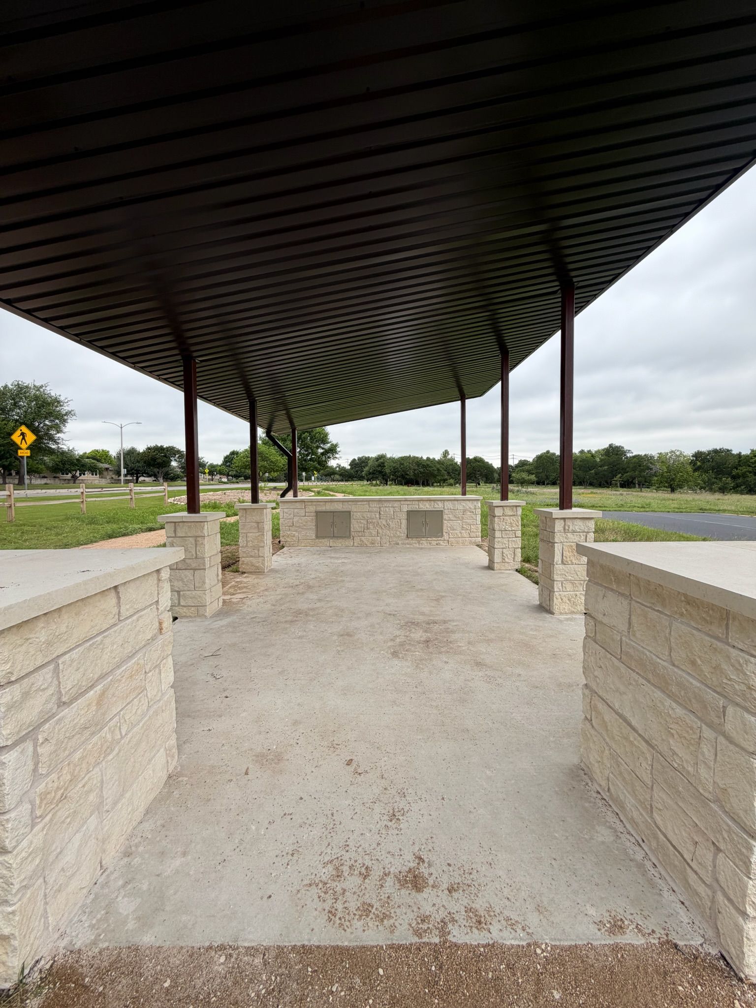 Covered stone walkway with curved black roof and gravel floor, opening to a roadside view.