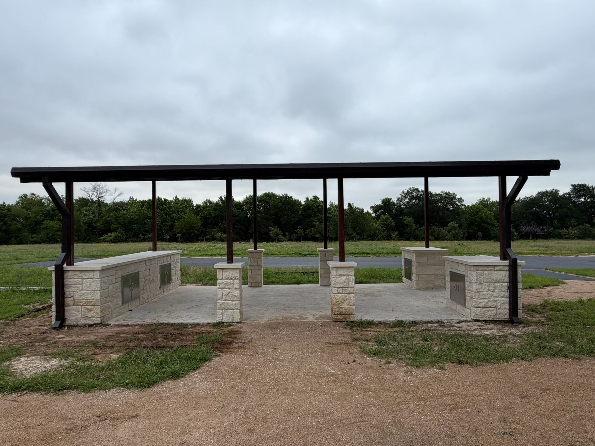 Outdoor picnic shelter with concrete benches and table under a cloudy sky on a gravel path