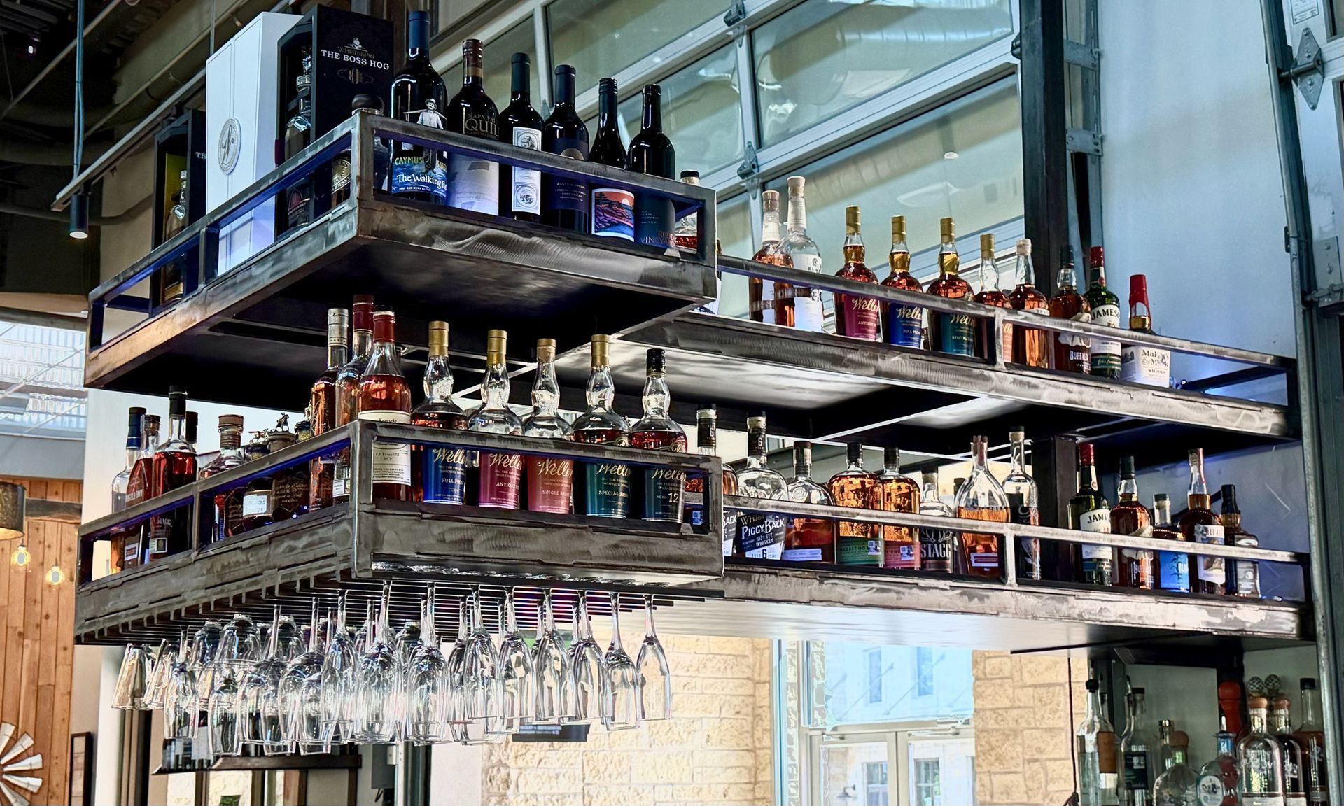Suspended bar shelves stocked with liquor bottles and hanging wine glasses in a modern restaurant