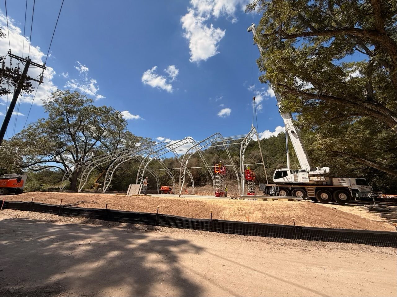 Construction site with a crane lifting materials on a dirt lot under a blue sky.