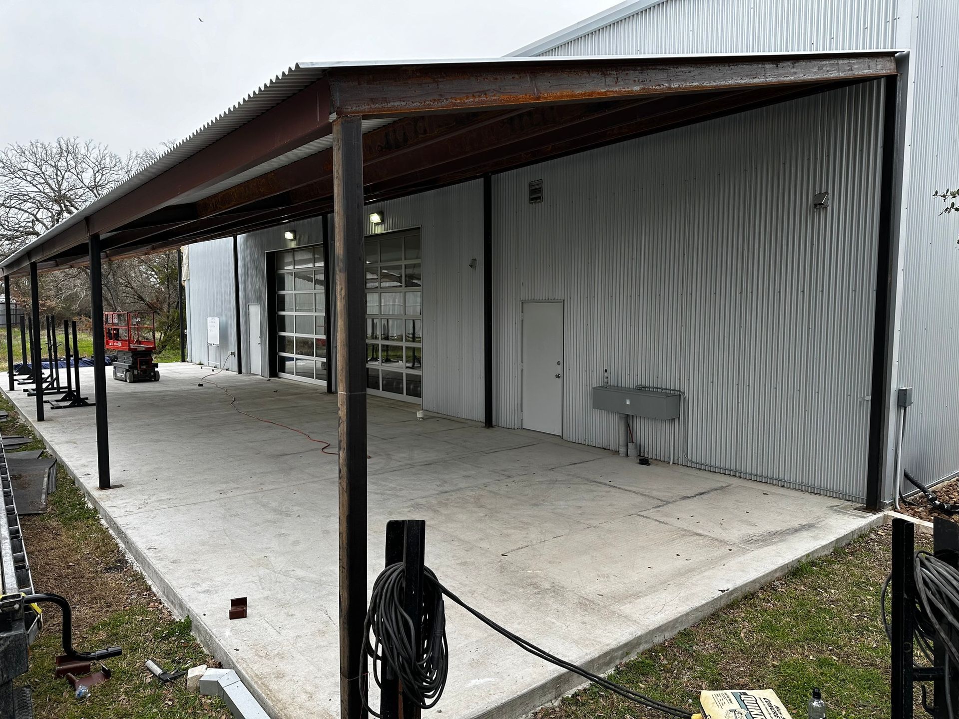 Metal awning over a concrete patio, attached to a corrugated metal building with glass doors.
