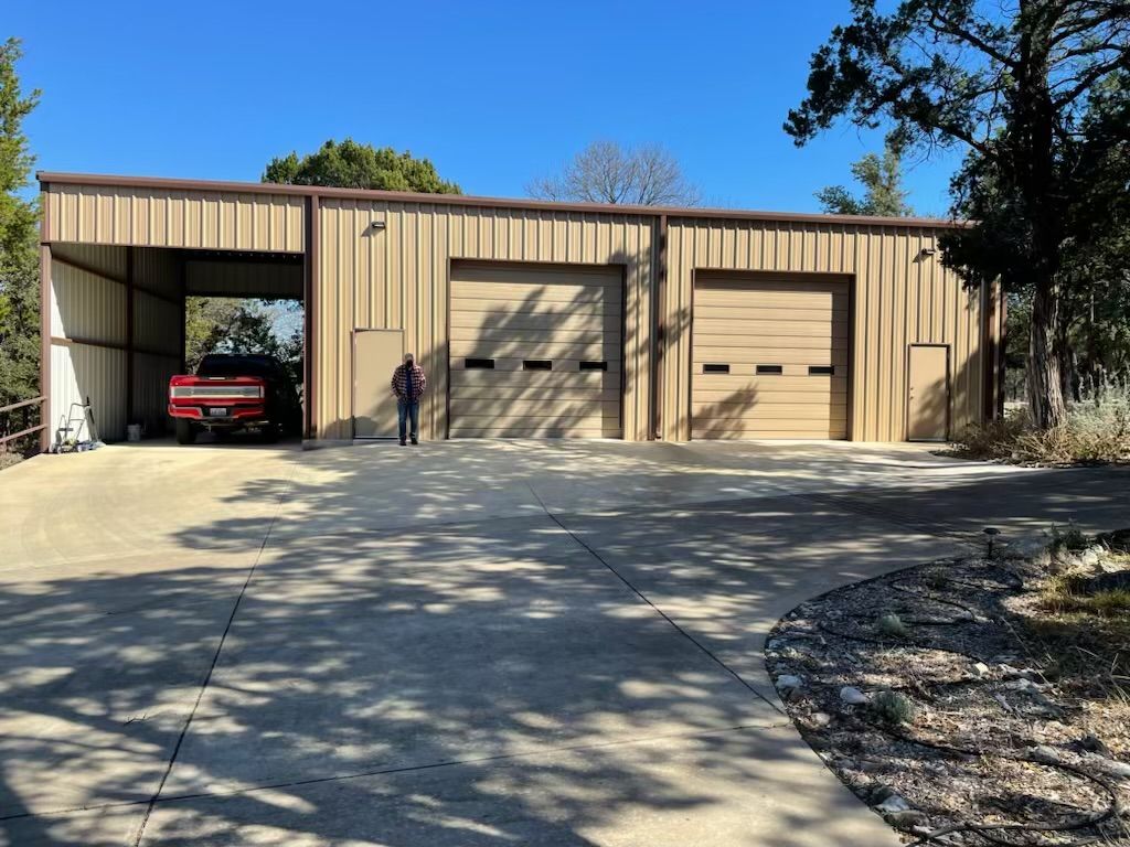A tan metal building with two garage doors and a car inside a covered bay. A person stands in front.