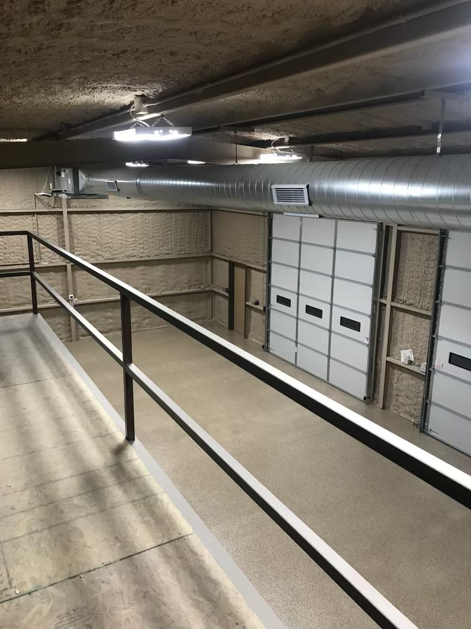 Ramp with a black handrail overlooking an interior space with white doors, ductwork, and exposed ceiling.