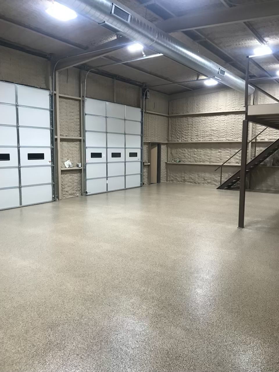 Empty warehouse interior with two garage doors, polished floor, and mezzanine.