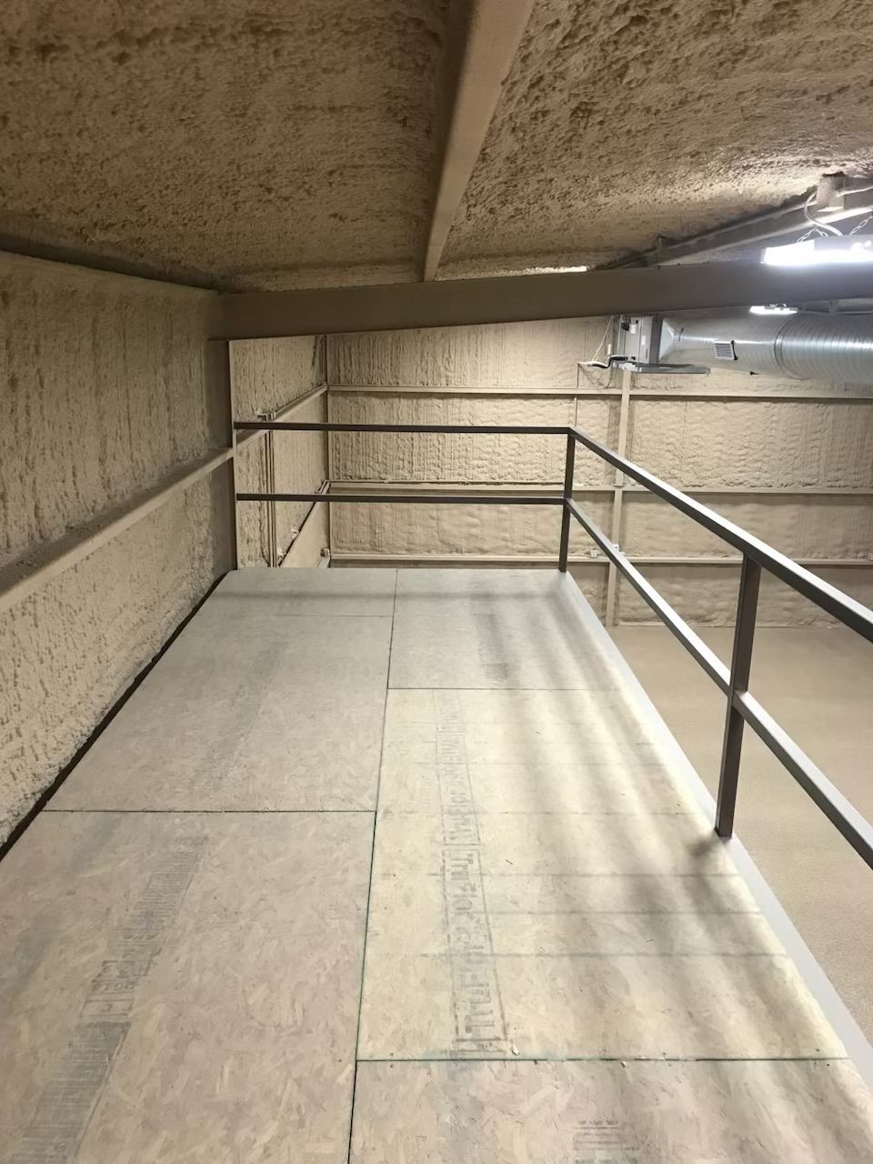 A narrow hallway with tan walls and a gray platform with a railing; an industrial setting.