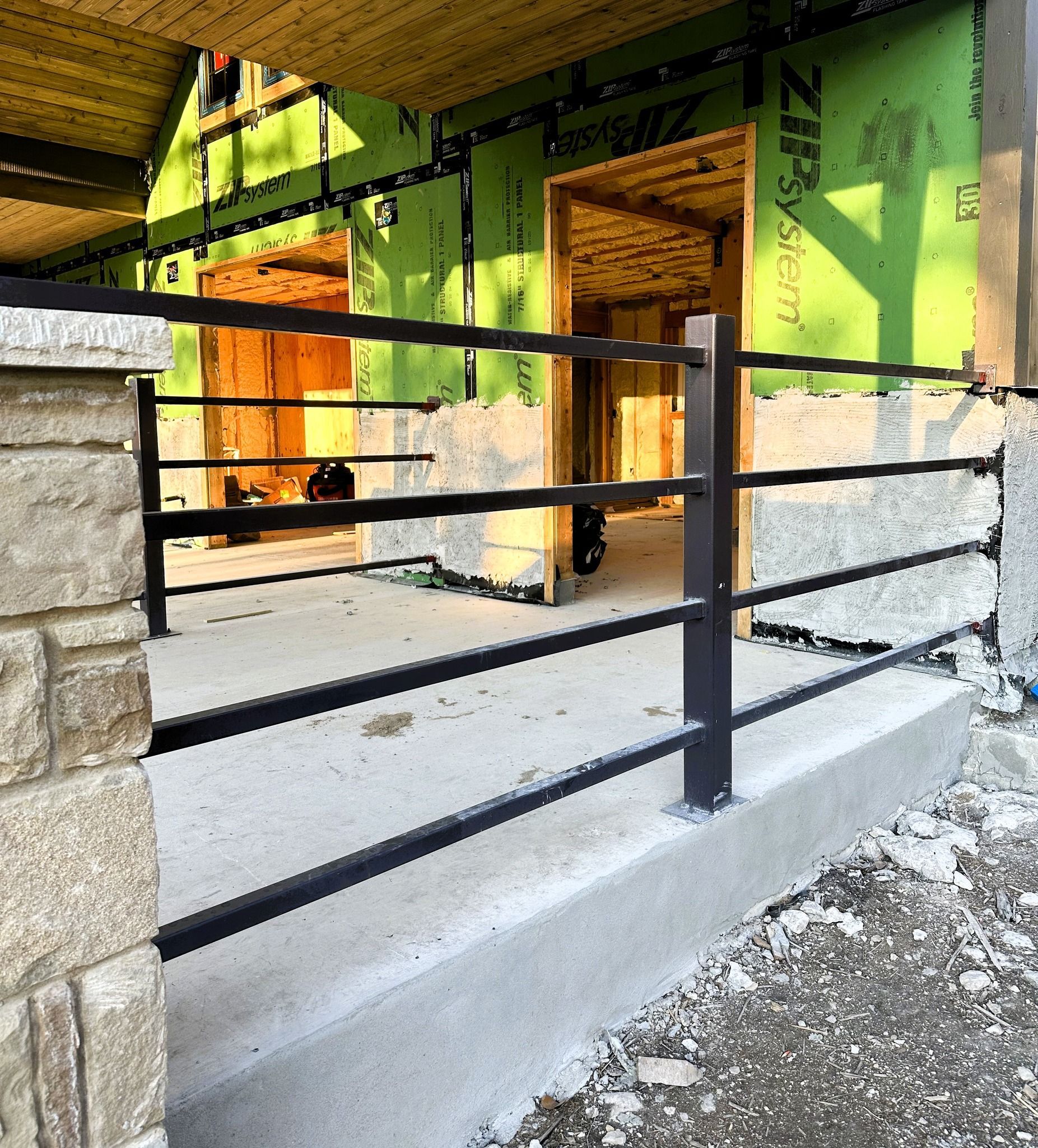 Black metal railing on a cement porch, beige stone wall on the left, doorway in the background.