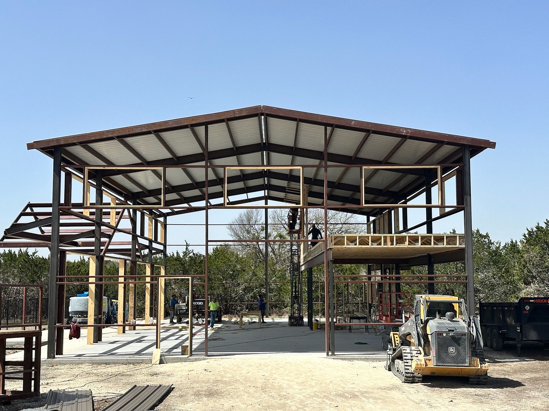 Construction of a metal building with brown roof and frame, in a gravel lot, on a sunny day.