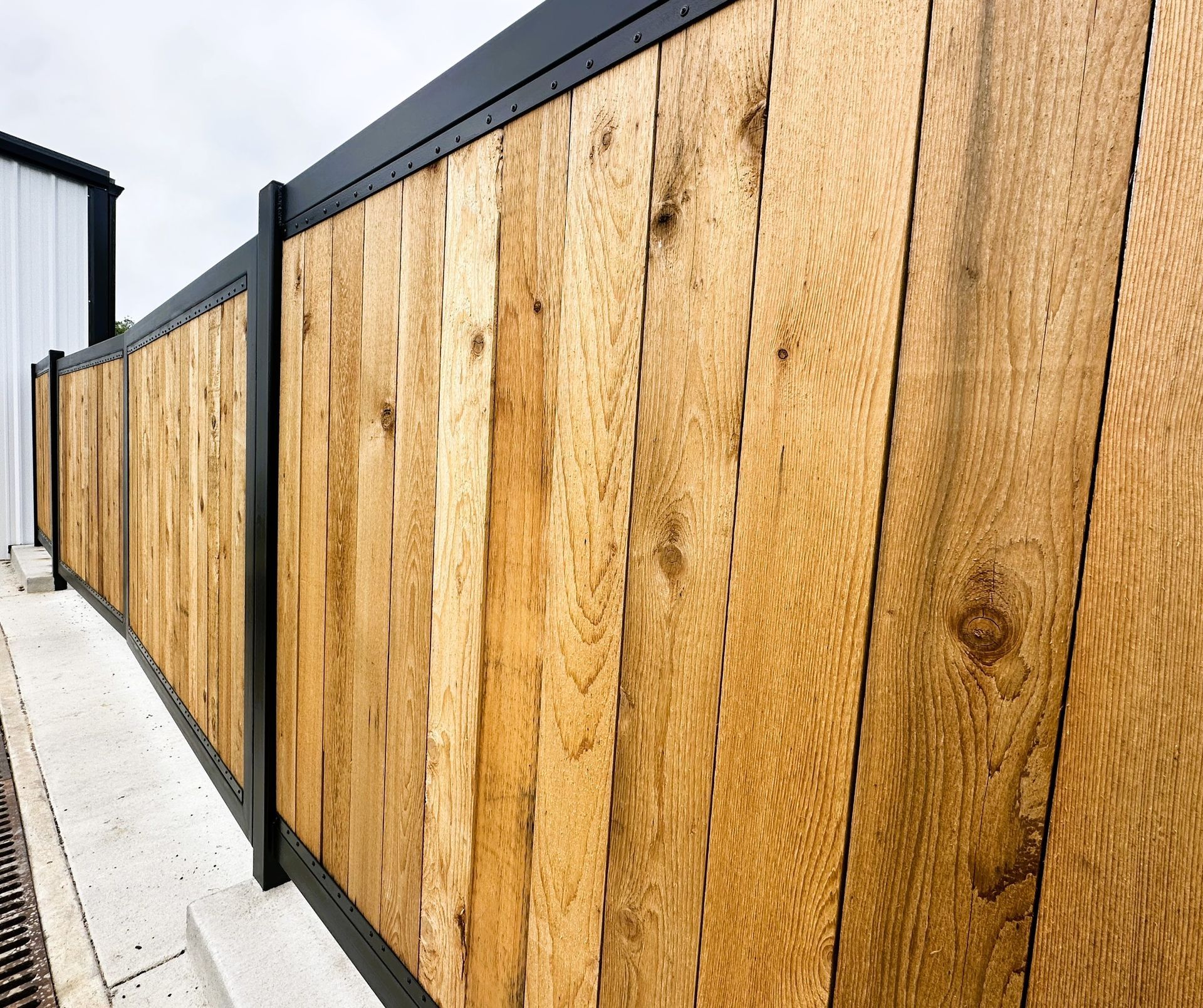 Wooden fence with dark metal frame. Exterior, daylight.