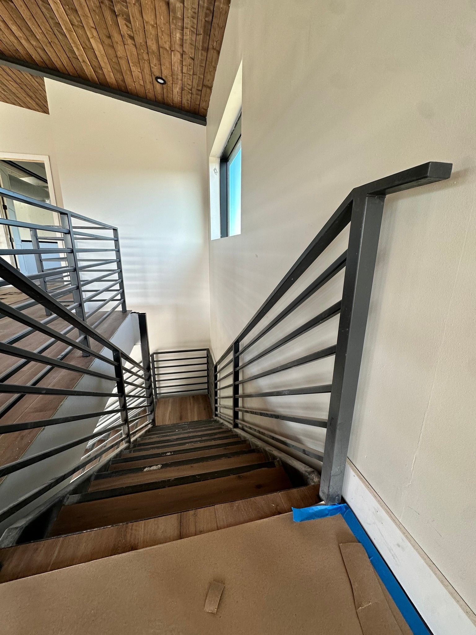 Interior view of a modern staircase with metal railings, wooden steps, and natural light.