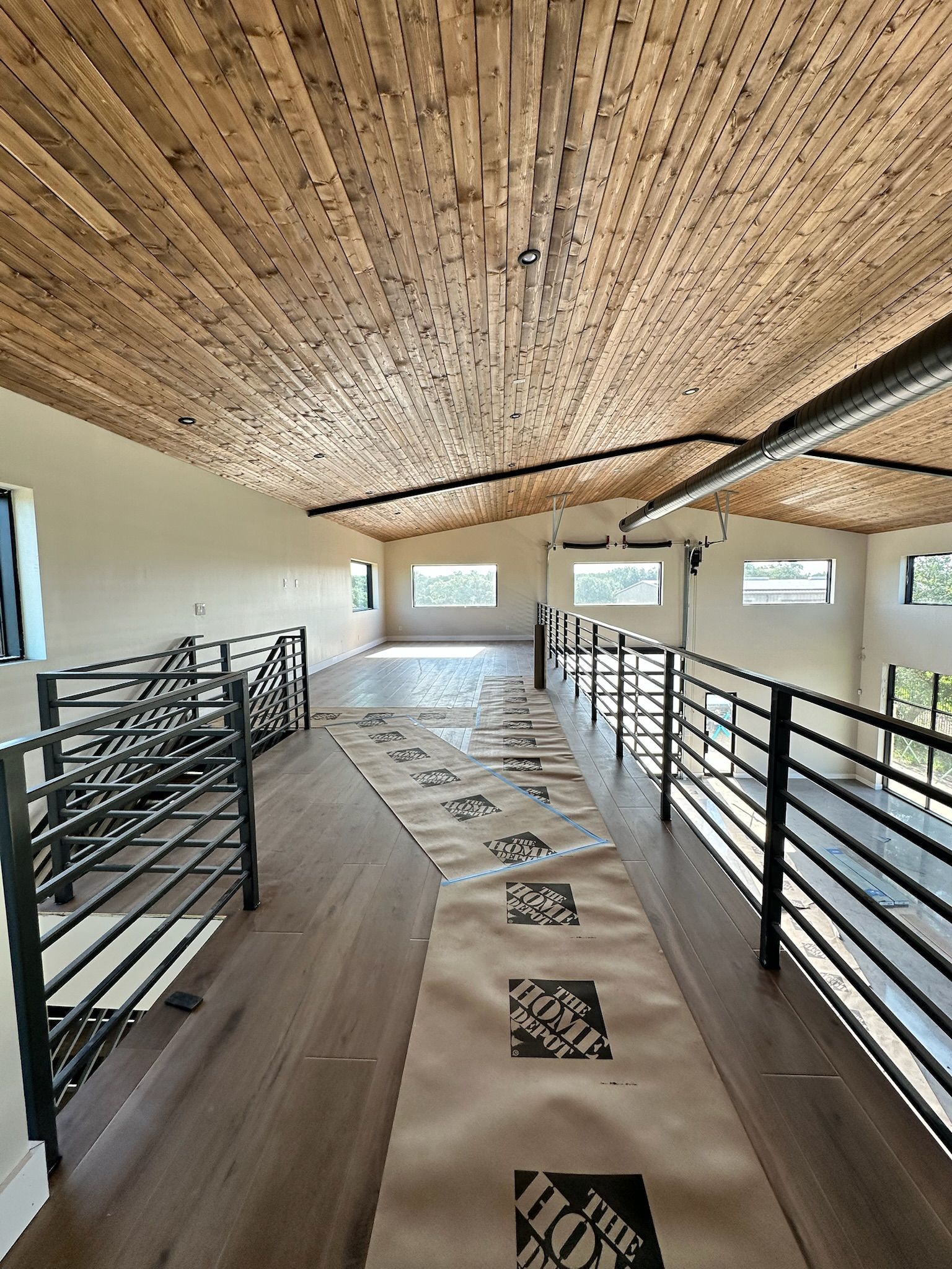 Interior view of a loft with a wood ceiling, wood floor, and black metal railings.