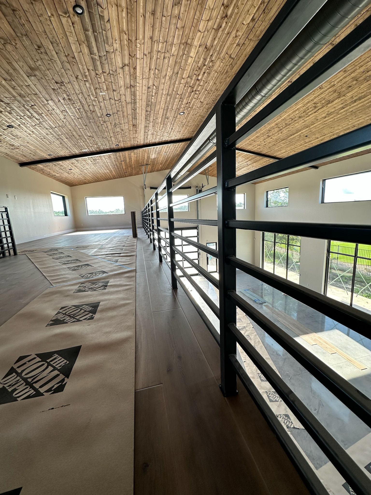 Interior view of a modern building with a balcony overlooking a spacious room. Black metal railing, bamboo ceiling.