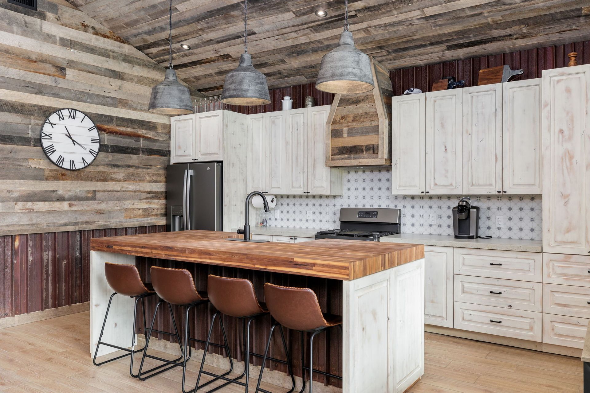 Rustic kitchen with white cabinets, wood countertop, island with stools, and three pendant lights.