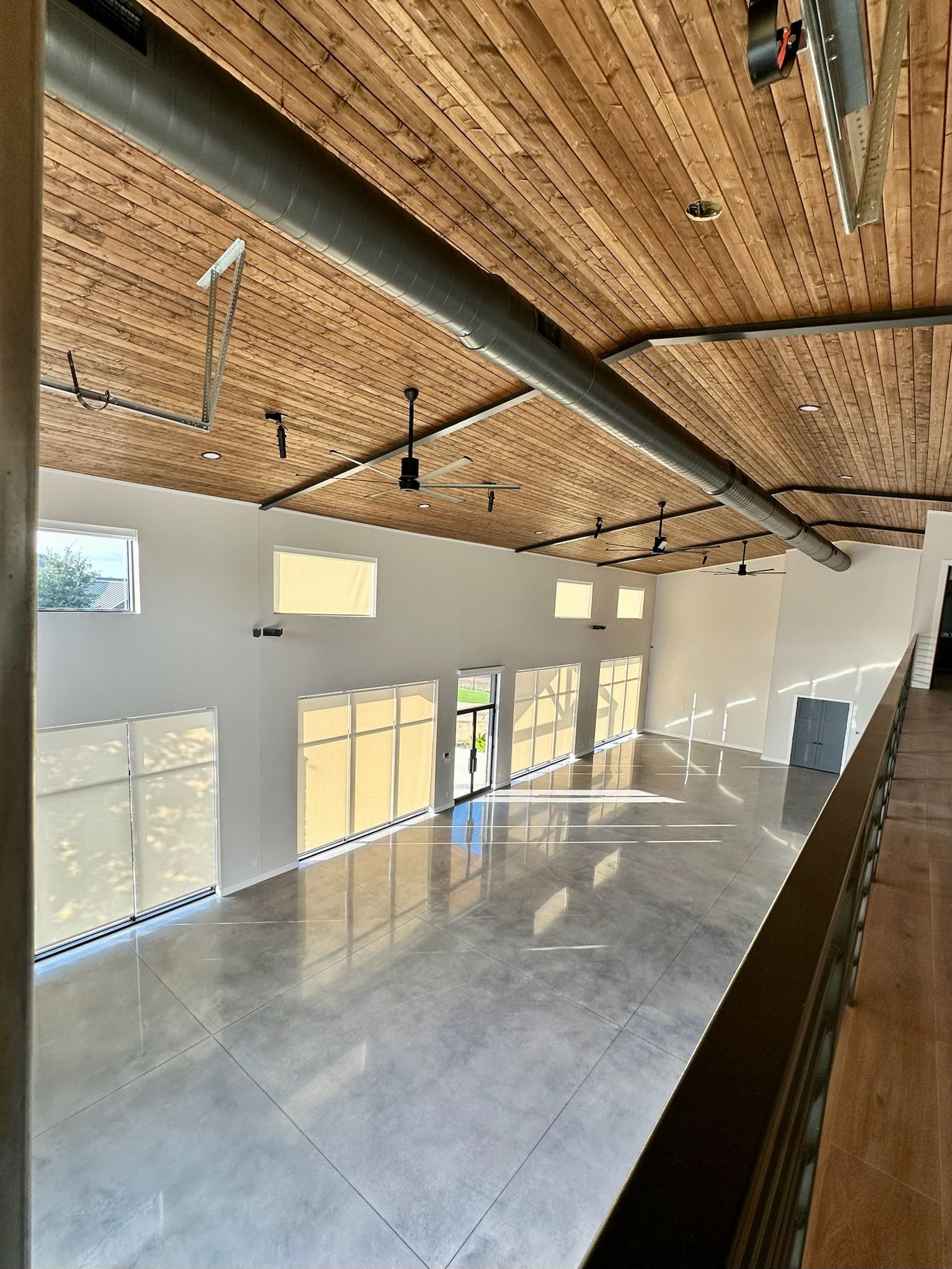 Interior shot of a large room with a polished concrete floor, light walls, wooden ceiling, and tall windows.
