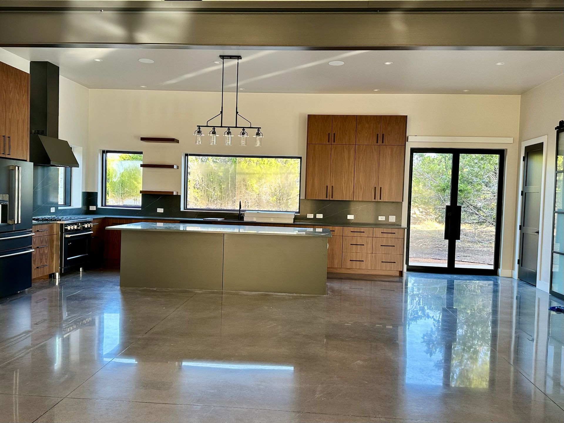 Modern kitchen with a large island, wooden cabinets, and polished concrete floor.