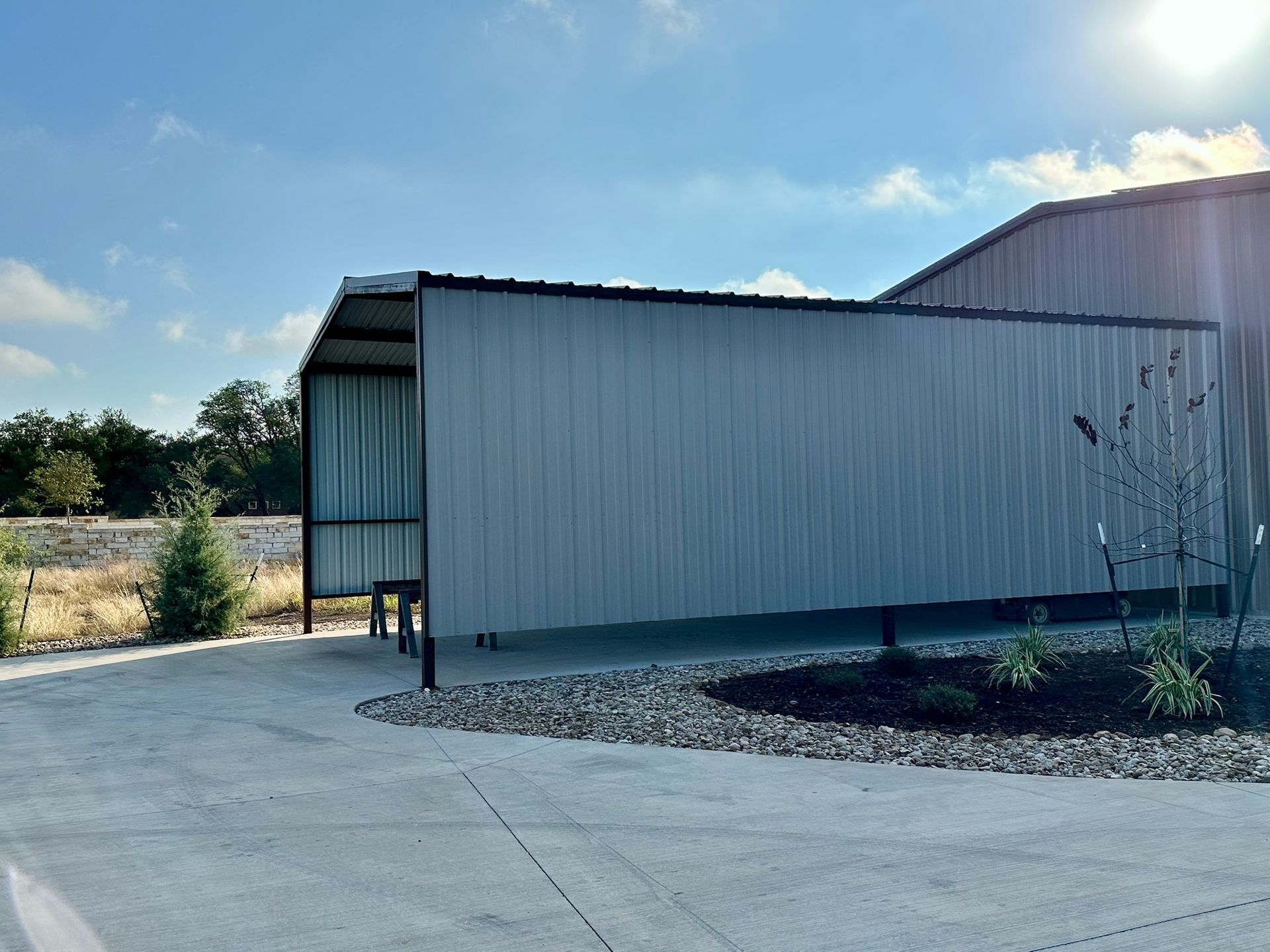 Metal building with a covered awning on a sunny day. Concrete drive and landscaping in front.