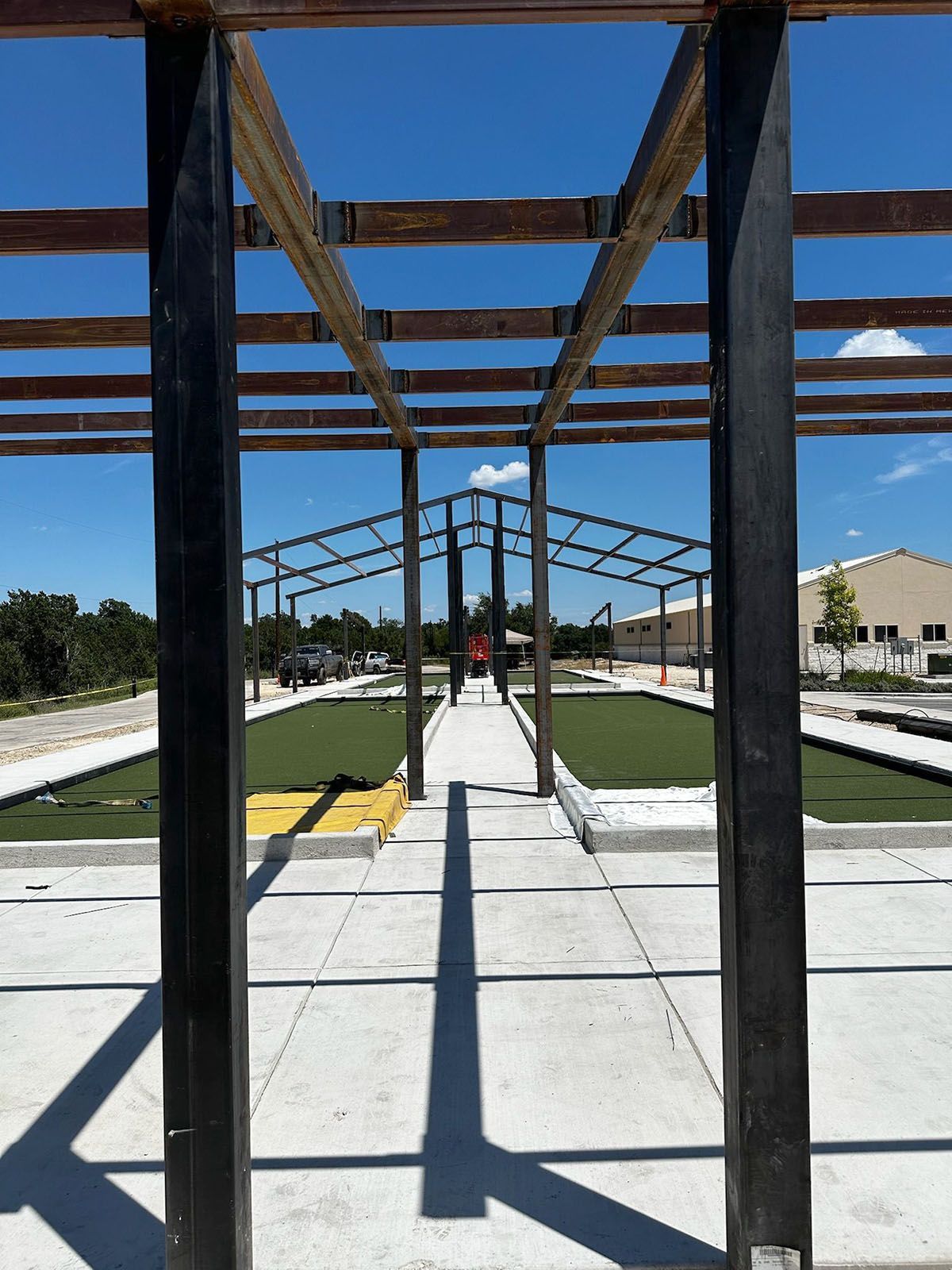 A wooden structure frames a pathway over a green artificial lawn, under a bright blue sky