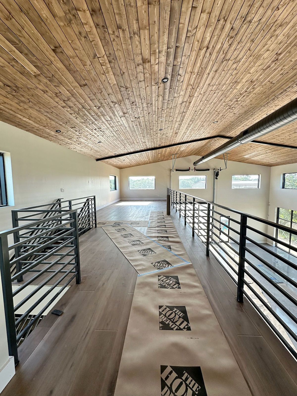 Interior of a loft with wood ceiling, metal railing, and windows
