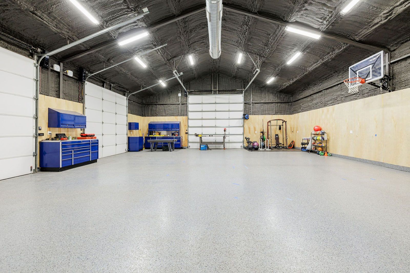 Spacious garage with gray flooring, blue cabinets, basketball hoop, and open white doors