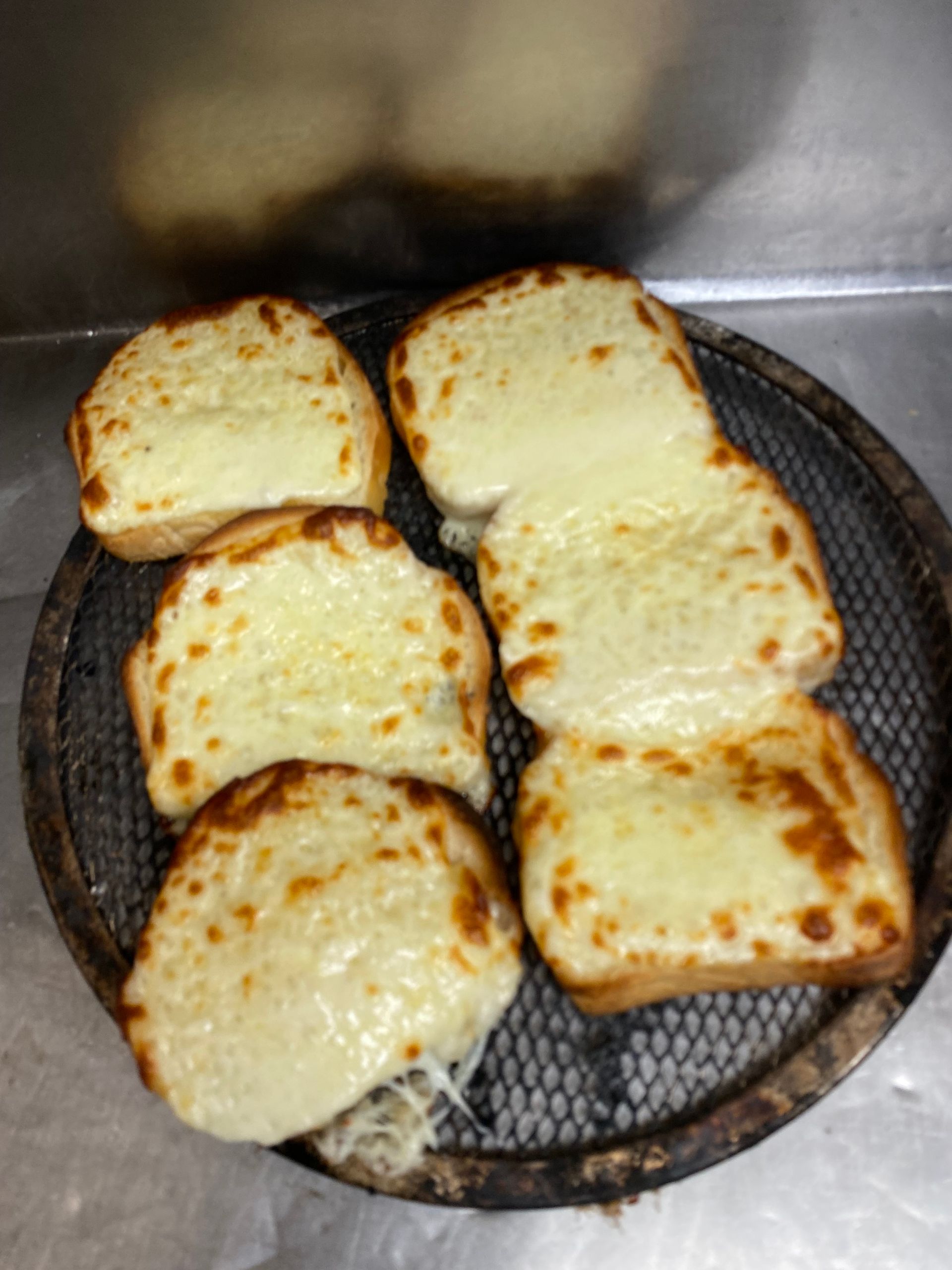 Five slices of cheesy garlic bread on a round metal wire tray.