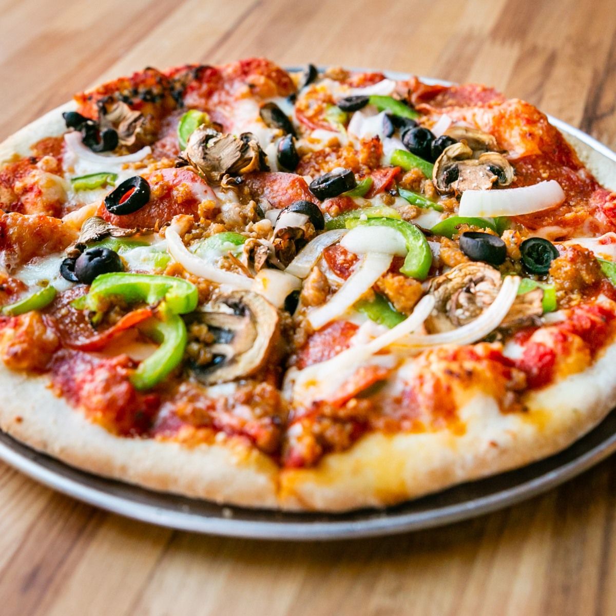 Pizza with various toppings on a metal tray, on a wooden surface.