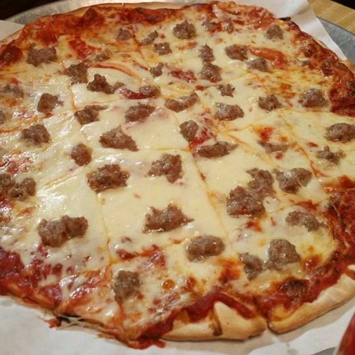 Pizza with sausage and cheese, cut into slices, on a pizza pan.
