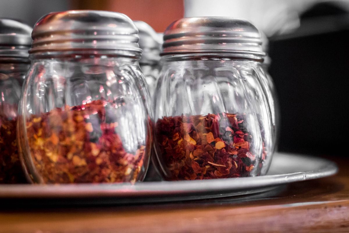 Glass jars filled with red pepper flakes sit on a metal tray.
