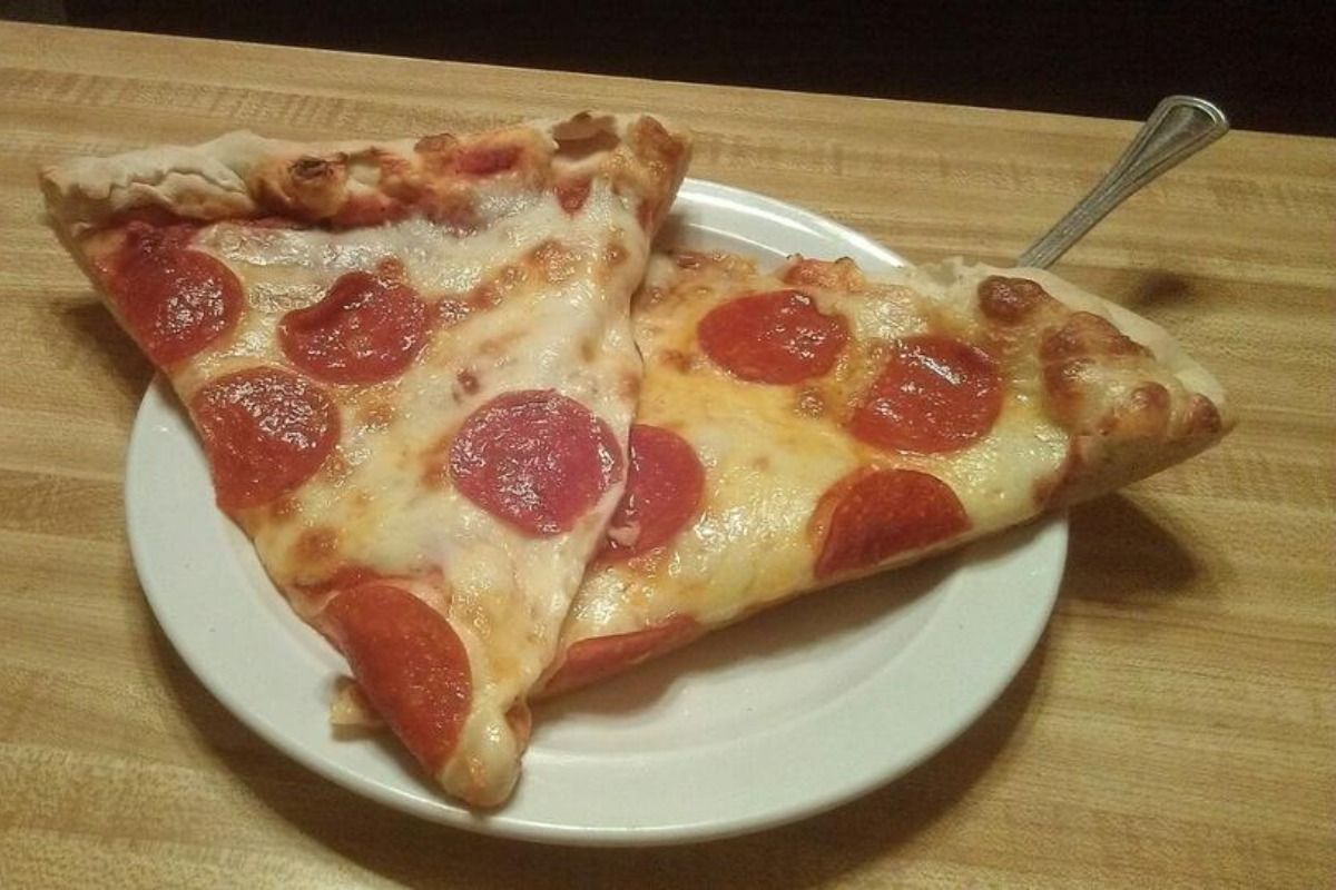 Two pepperoni pizza slices on a white plate; a fork sits nearby on a wooden surface.