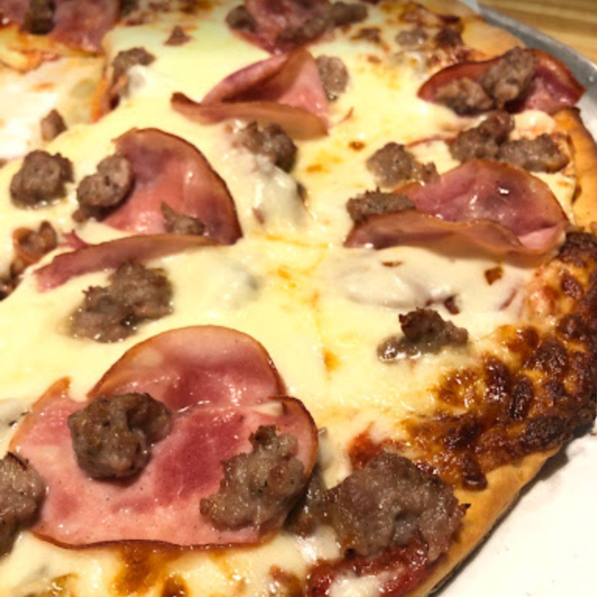 Pizza with sausage and ham toppings, close-up shot on a plate.
