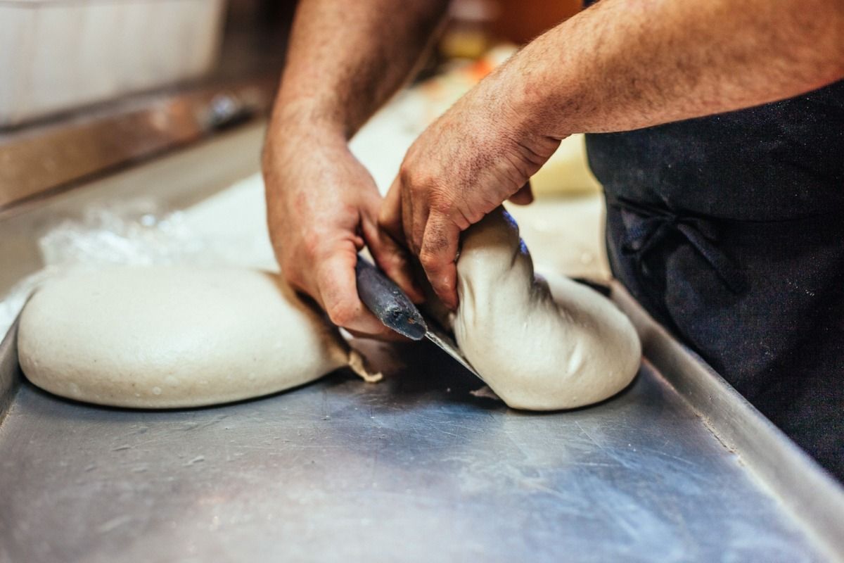 Hands cutting dough on a metal surface; dough is smooth and off-white.