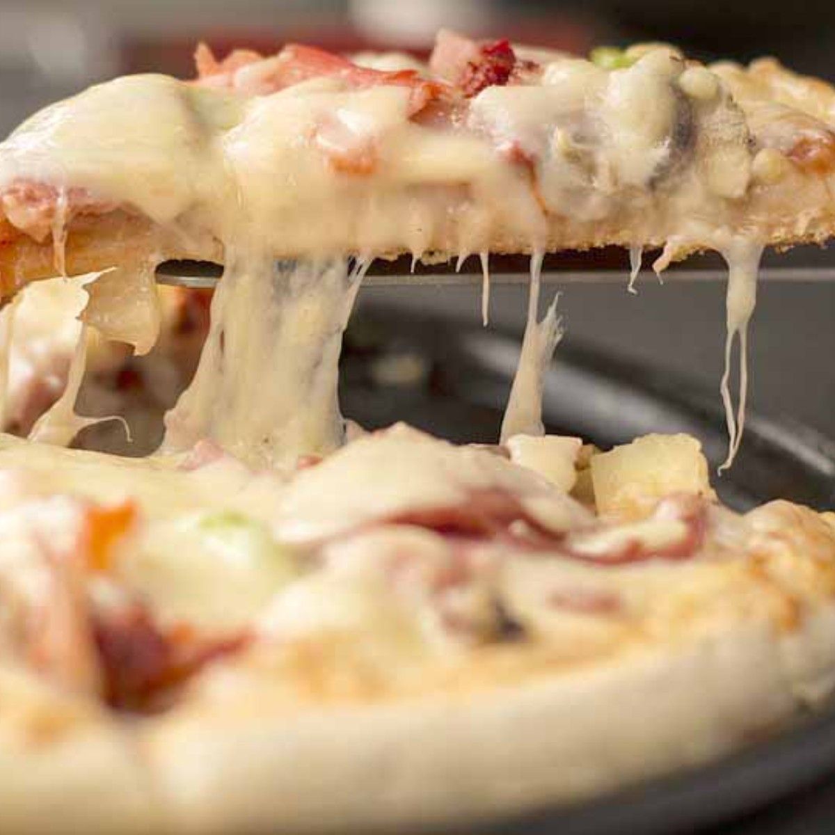 Slice of pizza with melted cheese being lifted, toppings visible.