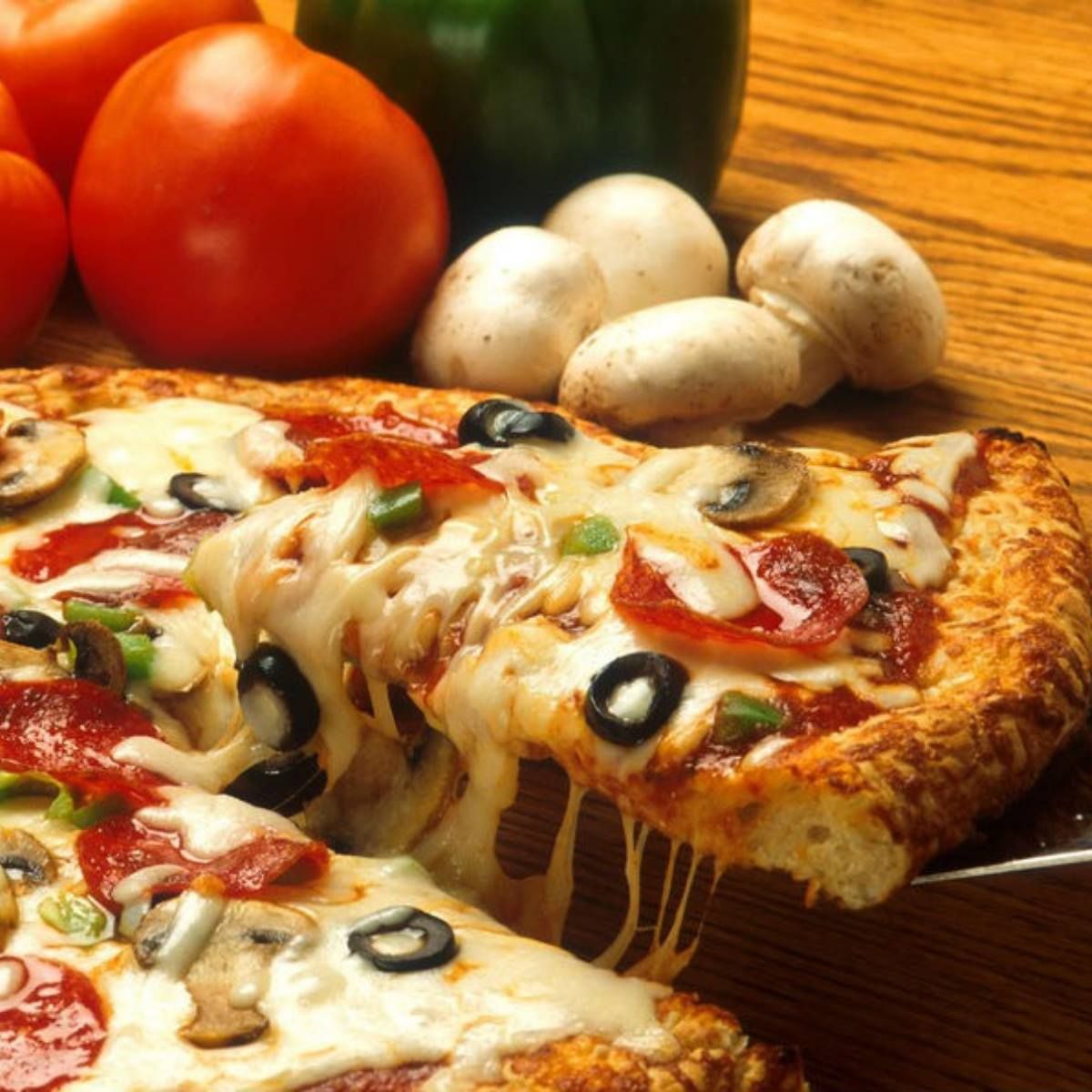 Pizza slice being lifted, showing melted cheese, pepperoni, olives, and mushrooms.