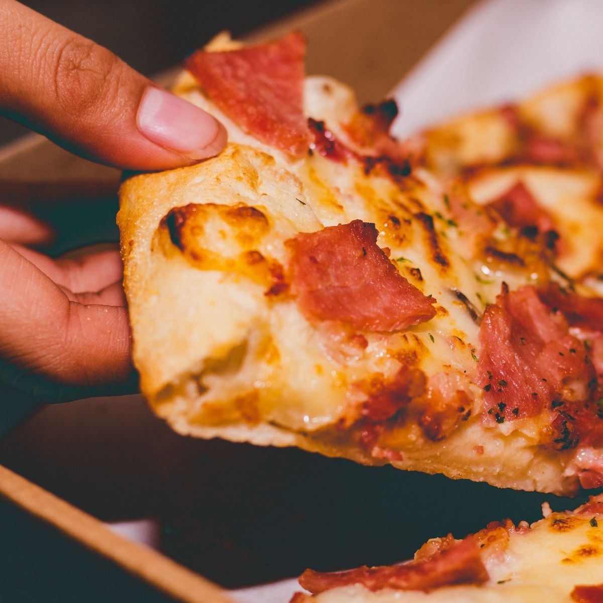 Hand holding a slice of pizza with meat toppings.