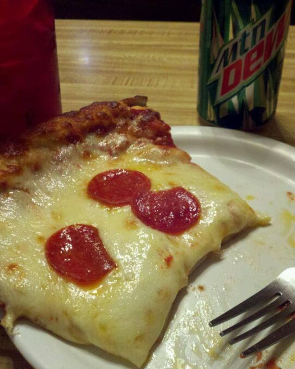 Slice of pepperoni pizza on a white plate with Mountain Dew and a red drink.