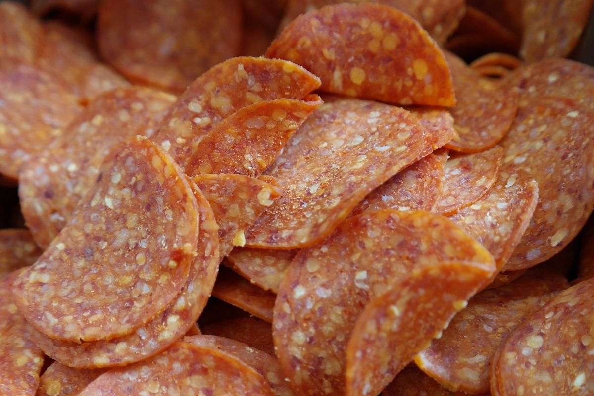 Pile of sliced pepperoni, reddish-orange in color.