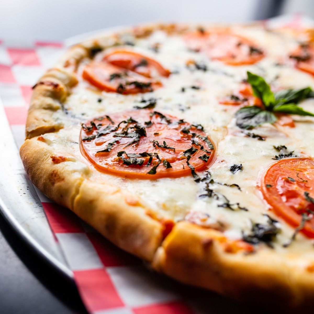 Pizza with tomato slices, basil, and cheese on a checkered paper-lined tray.
