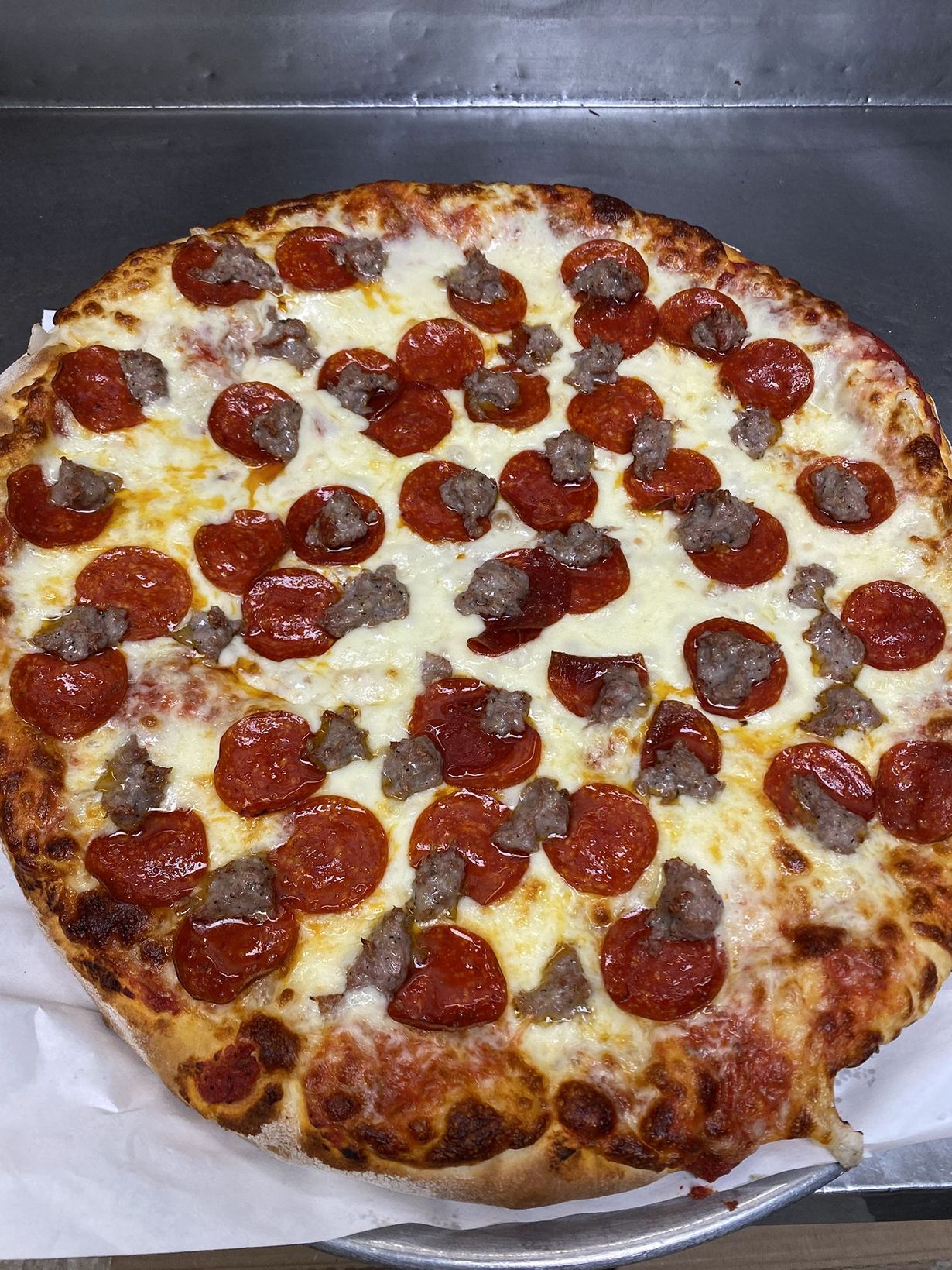 Pizza with tomatoes, basil, and cheese on a checkered paper on a metal tray.