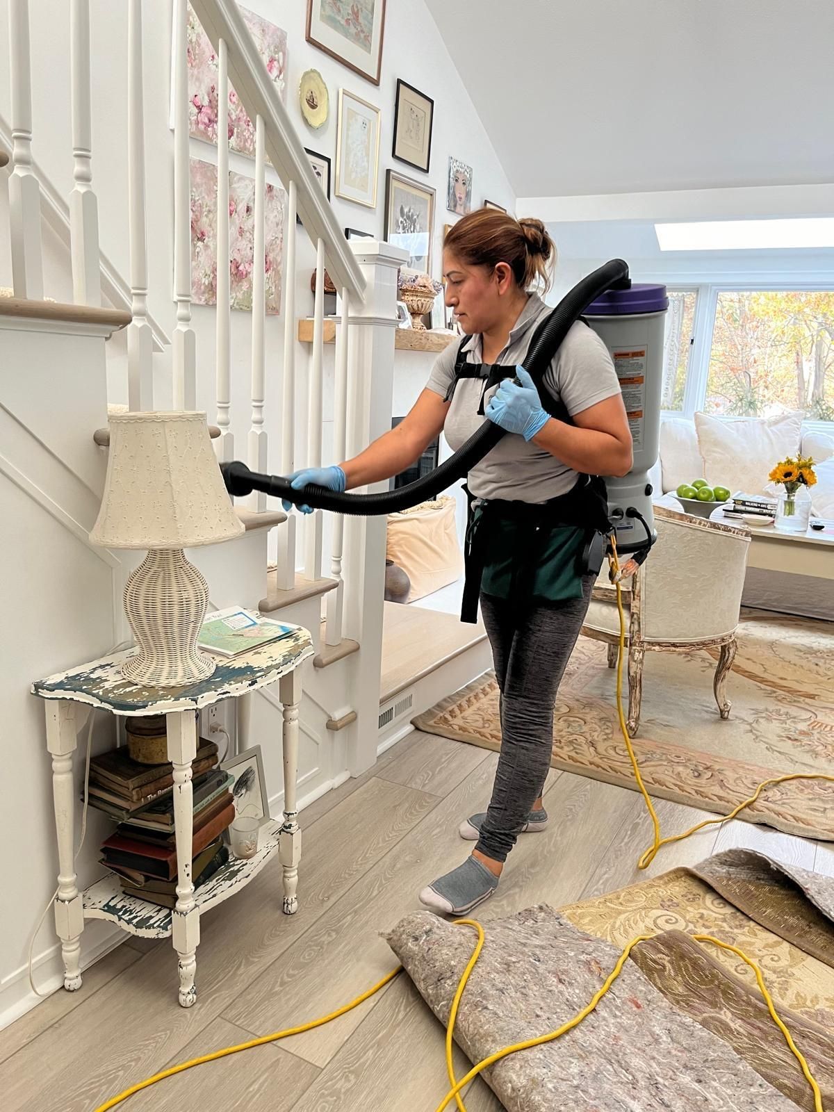 Woman vacuuming stairs with a backpack vacuum cleaner in a home.