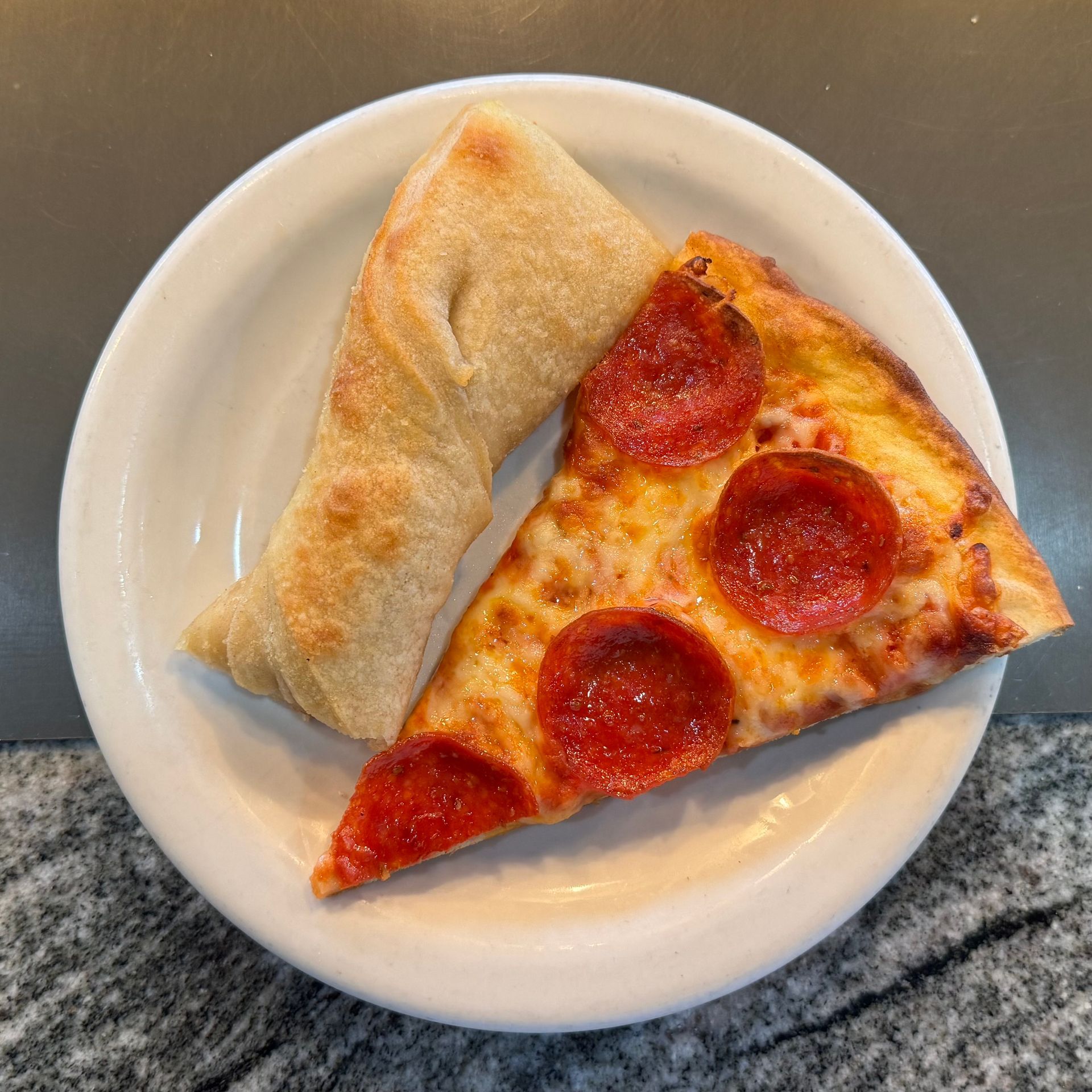 Pepperoni pizza slice and a folded pastry on a white plate