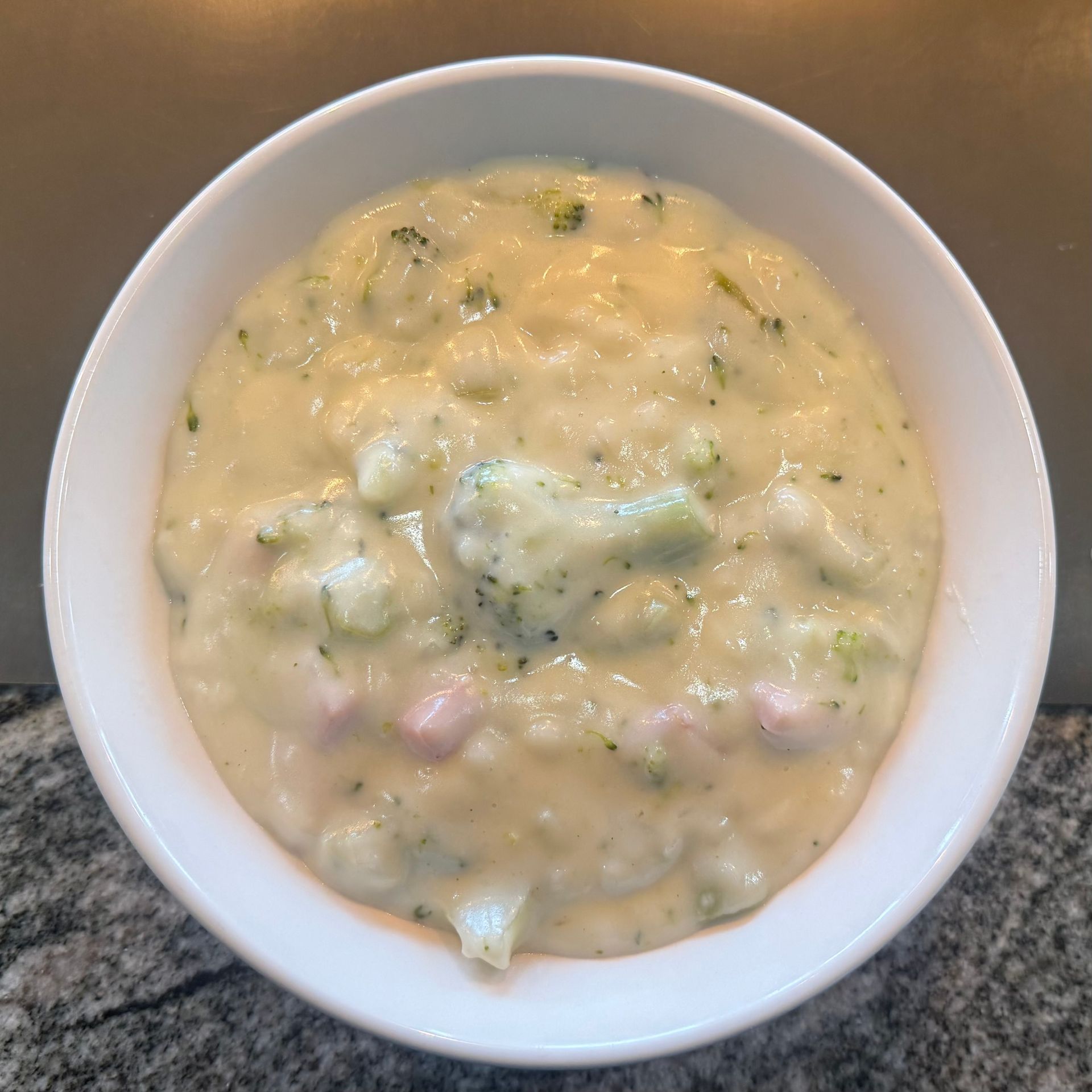 Bowl of creamy soup with green herbs and chunks, on a countertop